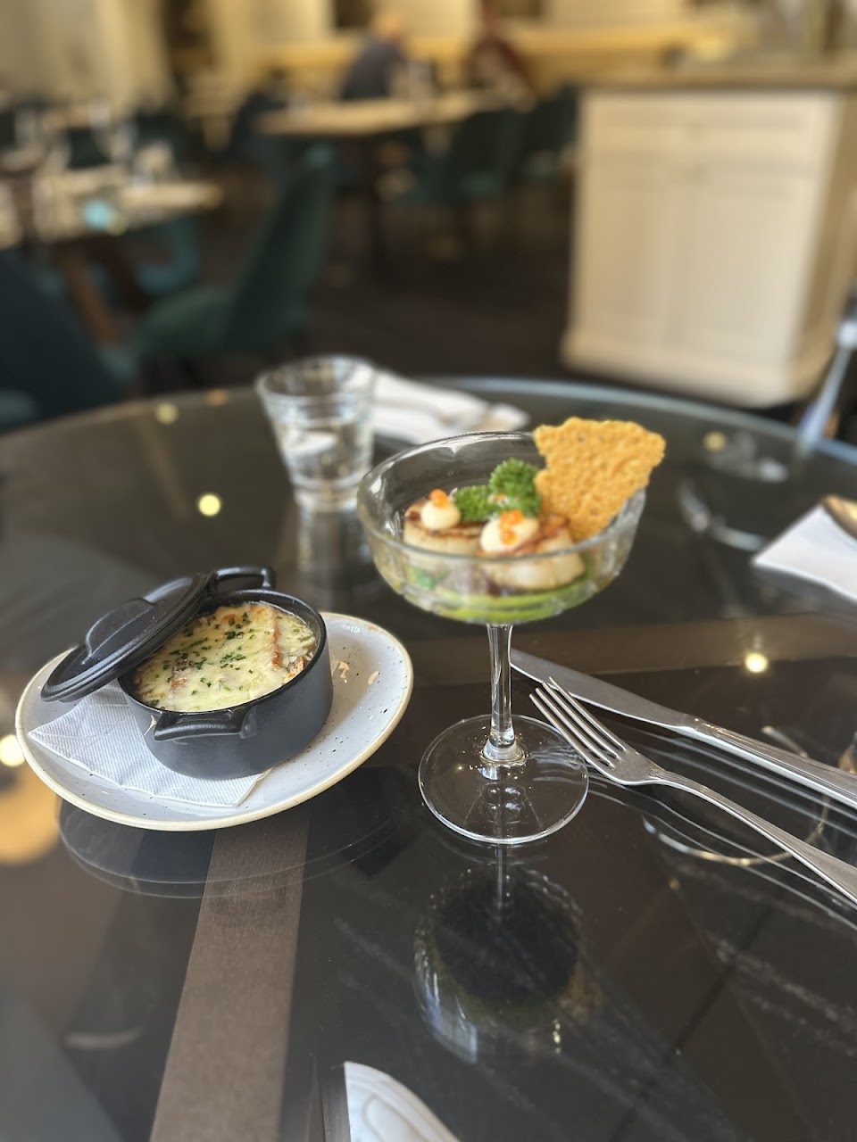 A scallop entree and baked side dish on a glass table